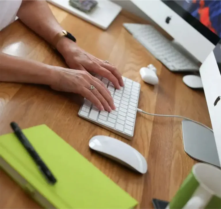Person typing at a desktop workstation with a notebook and computer equipment