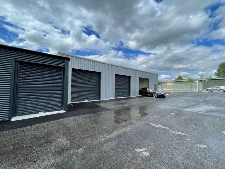Secure vehicle storage units with black roller doors and a parked car
